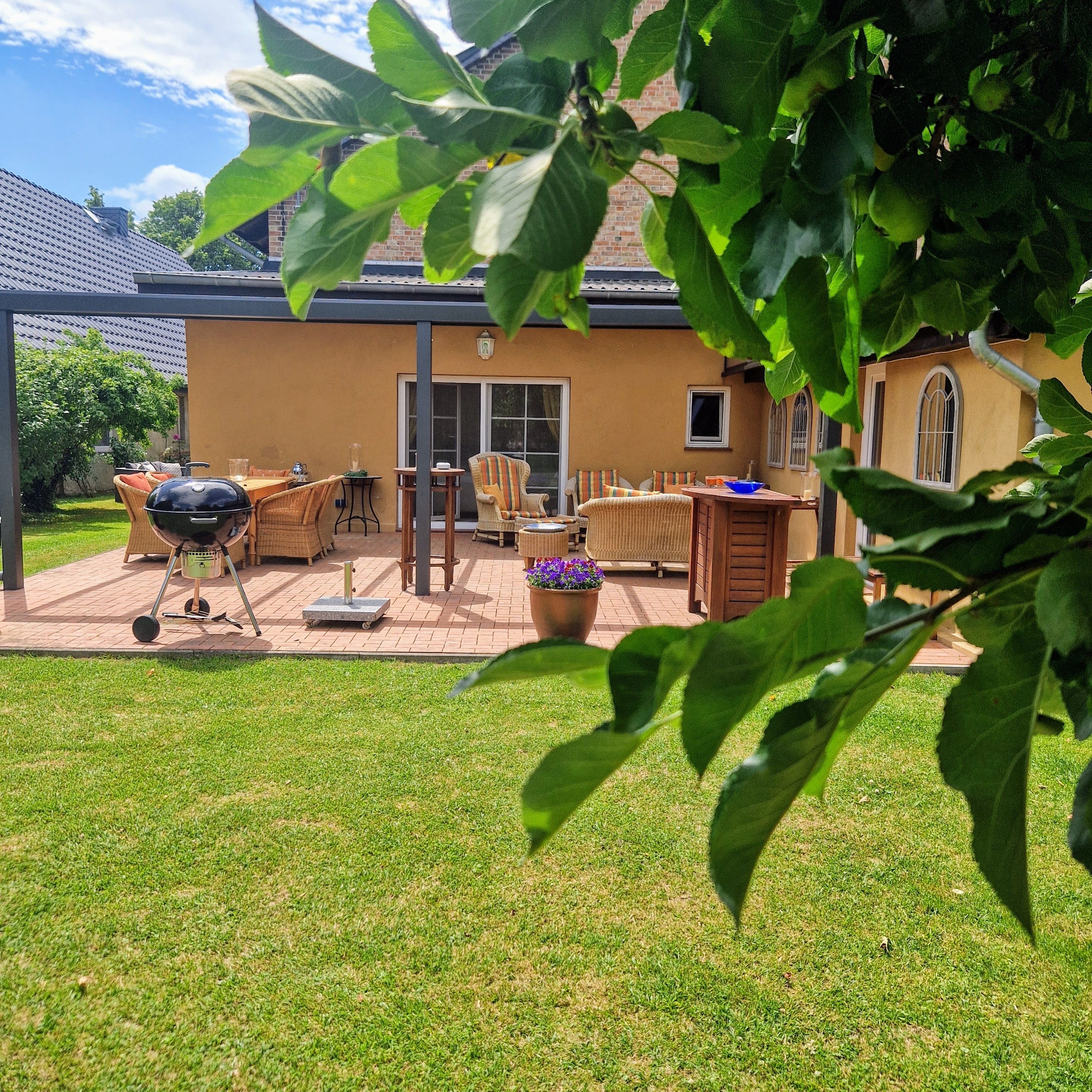 En patio med udendørs møbler, grill og en potteplante.