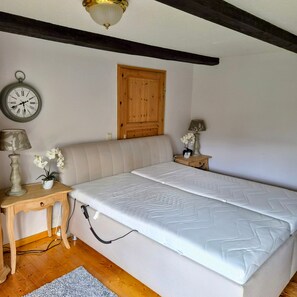 Ein Schlafzimmer mit einem Bett, einem Nachttisch aus Holz, einer Lampe, einer Wanduhr und einer Tür.
