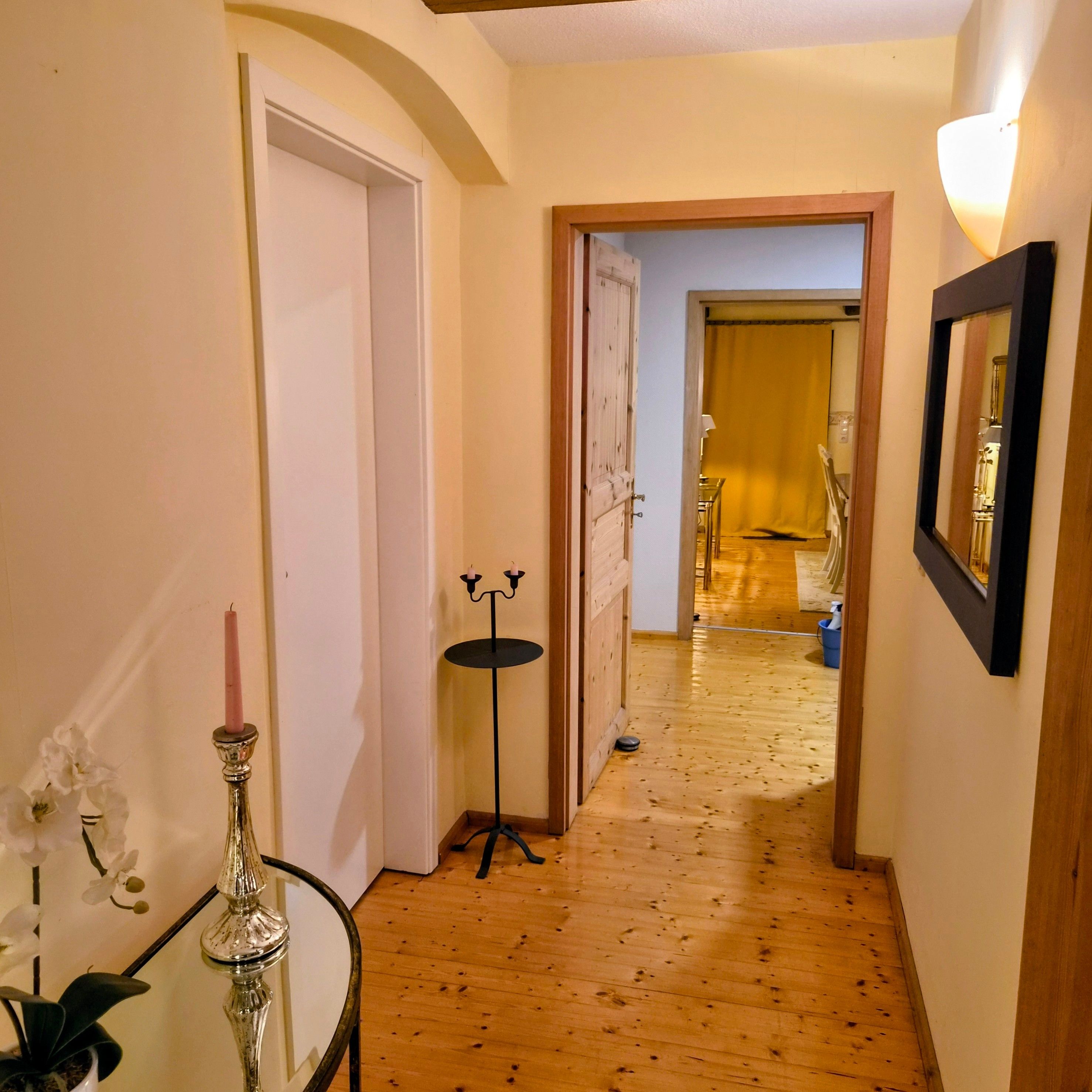 A hallway with wooden flooring, a white door, and a small table with a vase and candle.