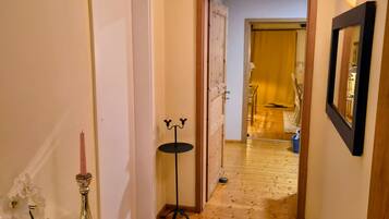 A hallway with wooden flooring, a white door, and a small table with a vase and candle.
