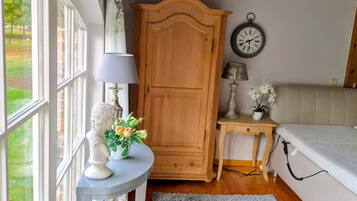 Una habitación con una cama, un armario de madera, un reloj de pared redondo, una mesita con una lámpara y un jarrón con flores.