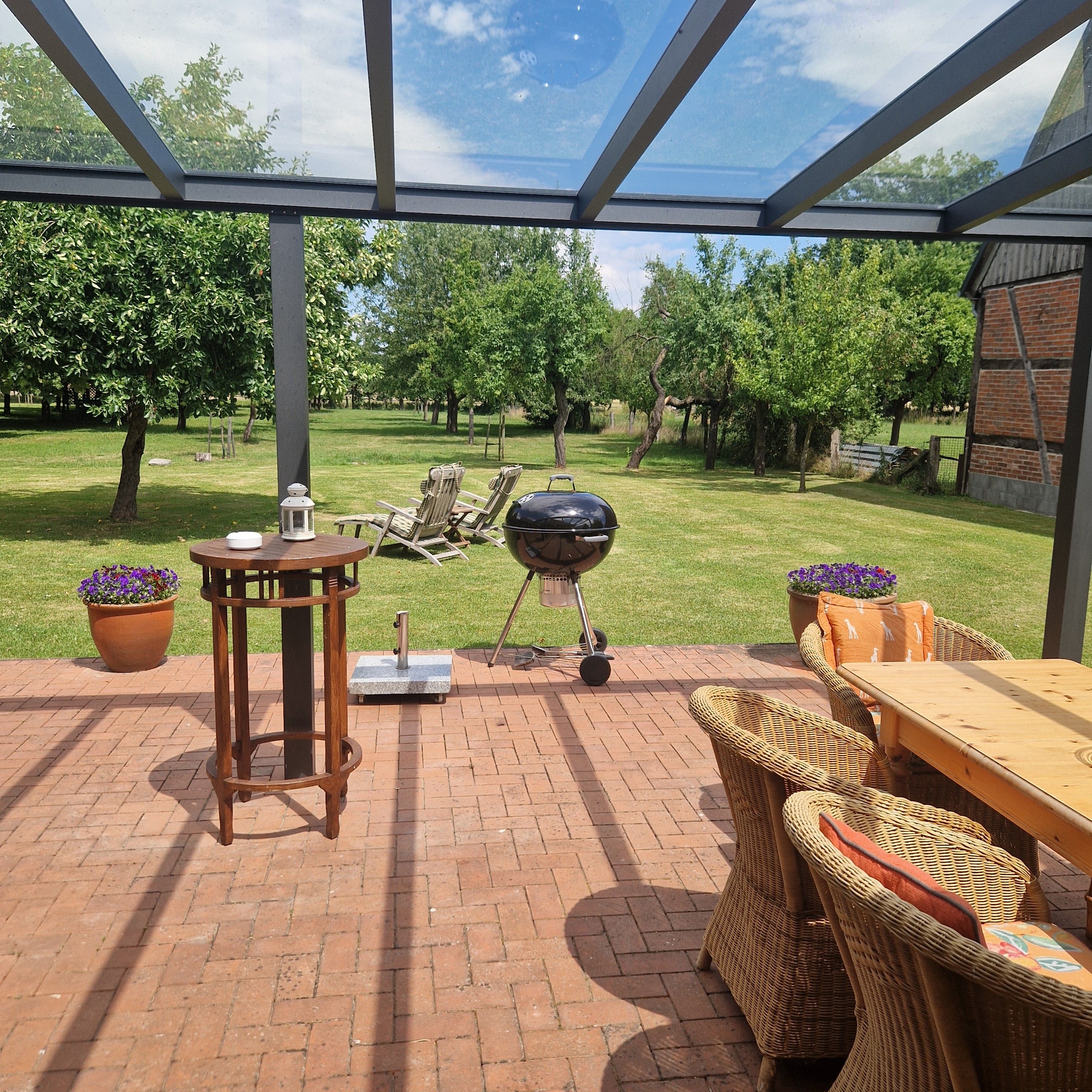 An outdoor patio with a grill, wicker furniture, and potted plants.
