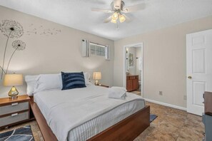 Une chambre à coucher avec un lit, des lampes de chevet, un ventilateur de plafond et une vue sur la salle de bain.