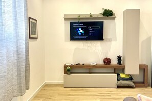 A modern living room with a flat-screen TV mounted on the wall, a wooden bench with cushions, and a small potted plant. - BNBOOK – Residenza Cavallotti 1 (Monza)