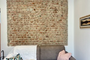 A room with a brick wall, a brown leather sofa, and a framed picture on the wall. - BNBOOK – Residenza Cavallotti 1 (Monza)