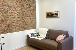 Een kamer met een bakstenen muur, een bruine bank, een ingelijst kunstwerk en een gestreept kussen.