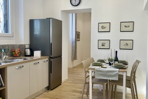 A modern kitchen with a refrigerator, sink, and dining area with chairs and a table set for two. - BNBOOK – Residenza Cavallotti 1 (Monza)