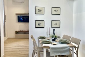 Een eetgedeelte met een gedekte tafel voor twee personen, kunstwerken aan de muur en een televisiescherm waarop een menu wordt weergegeven.