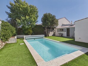 A rectangular swimming pool with a clear blue water surface, surrounded by a well-maintained lawn and a white building with a tiled roof in the background. - House for 6, pool & garden, walk everywhere (Noirmoutier-en-l´Ile)