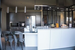 A modern kitchen with stainless steel appliances, a large island, and wicker chairs. - The House by the Pond in the Camargue (Arles)