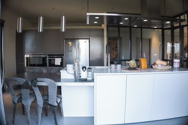A modern kitchen with stainless steel appliances, a large island, and wicker chairs. - The House by the Pond in the Camargue (Arles)