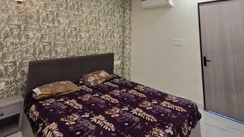 A bedroom with a bed, a ceiling fan, recessed lighting, an air conditioning unit, and patterned wallpaper.