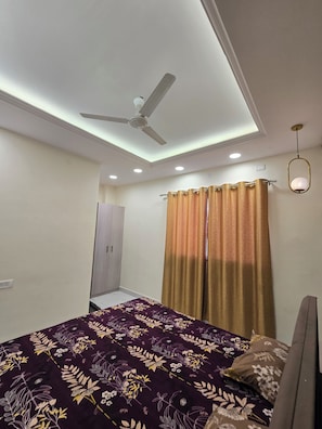 Un dormitorio con cama, ventilador de techo, luces empotradas, armario y ventana con cortinas.