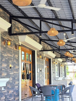 Un espacio al aire libre con mobiliario de mimbre, iluminación colgante y una estructura de techo de metal.
