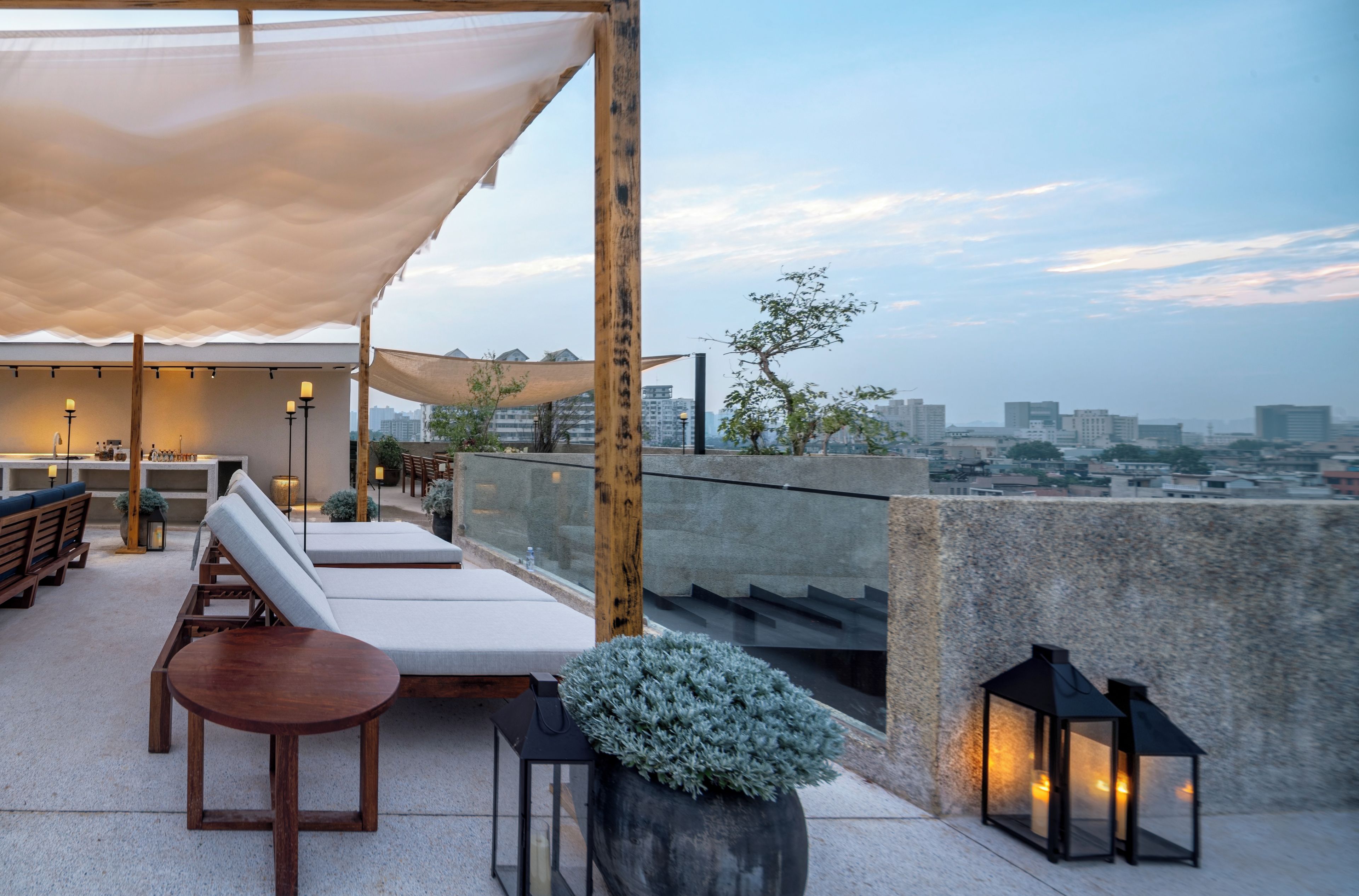 A rooftop terrace with lounge chairs, a table, and potted plants.