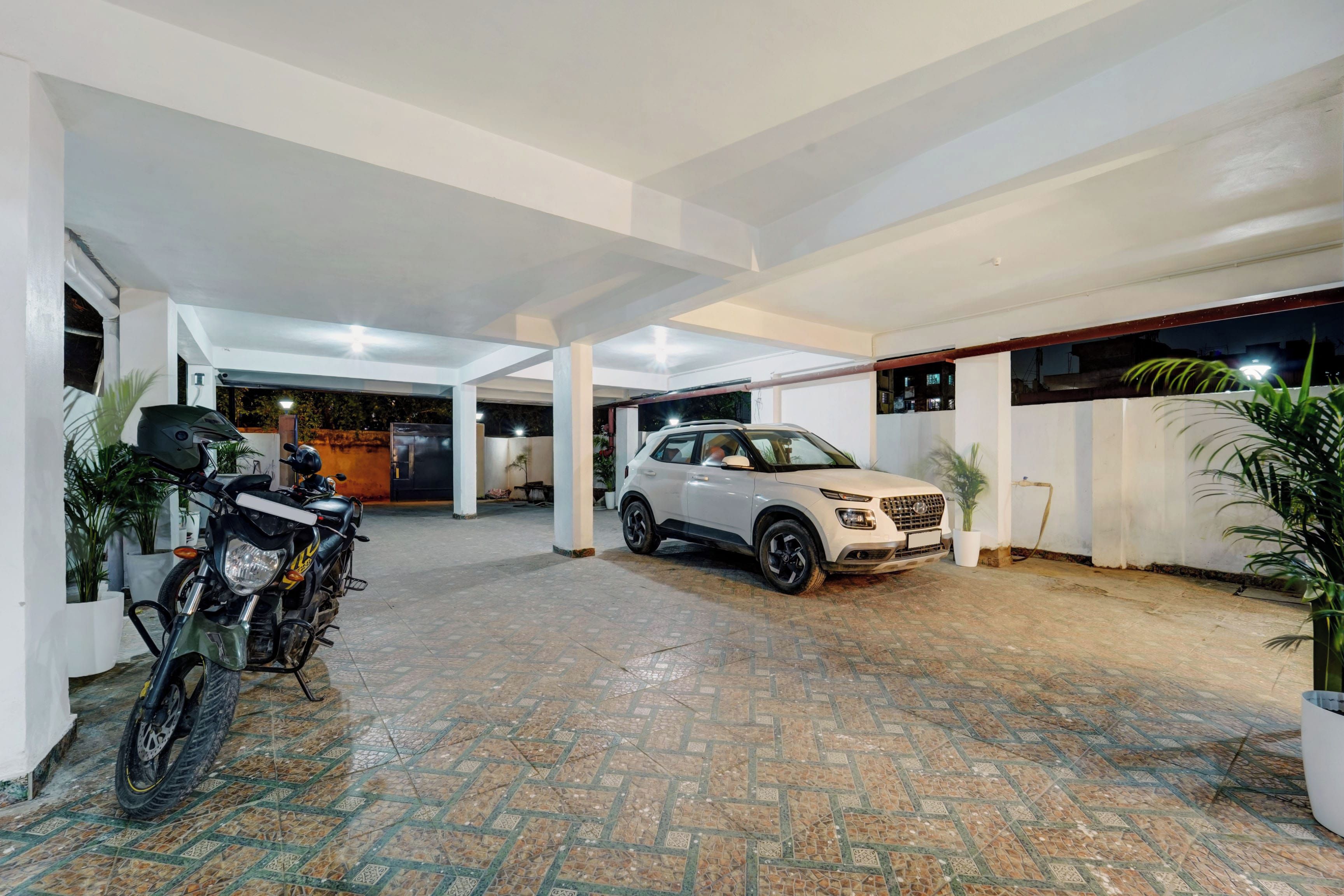 Un área de estacionamiento techada con un vehículo SUV blanco y una motocicleta.
