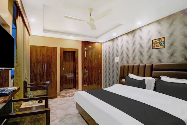 Habitación de hotel con cama, televisor, escritorio, armario y ventilador de techo.