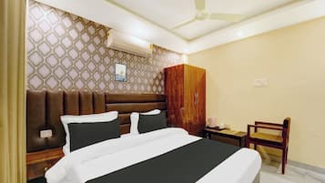 A hotel room with a bed, a wardrobe, a chair, a bedside table, and a ceiling fan.