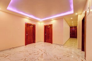 A hallway with marble flooring, wooden doors, and recessed ceiling lighting. - Hotel O The Dev Regency  (Patna)