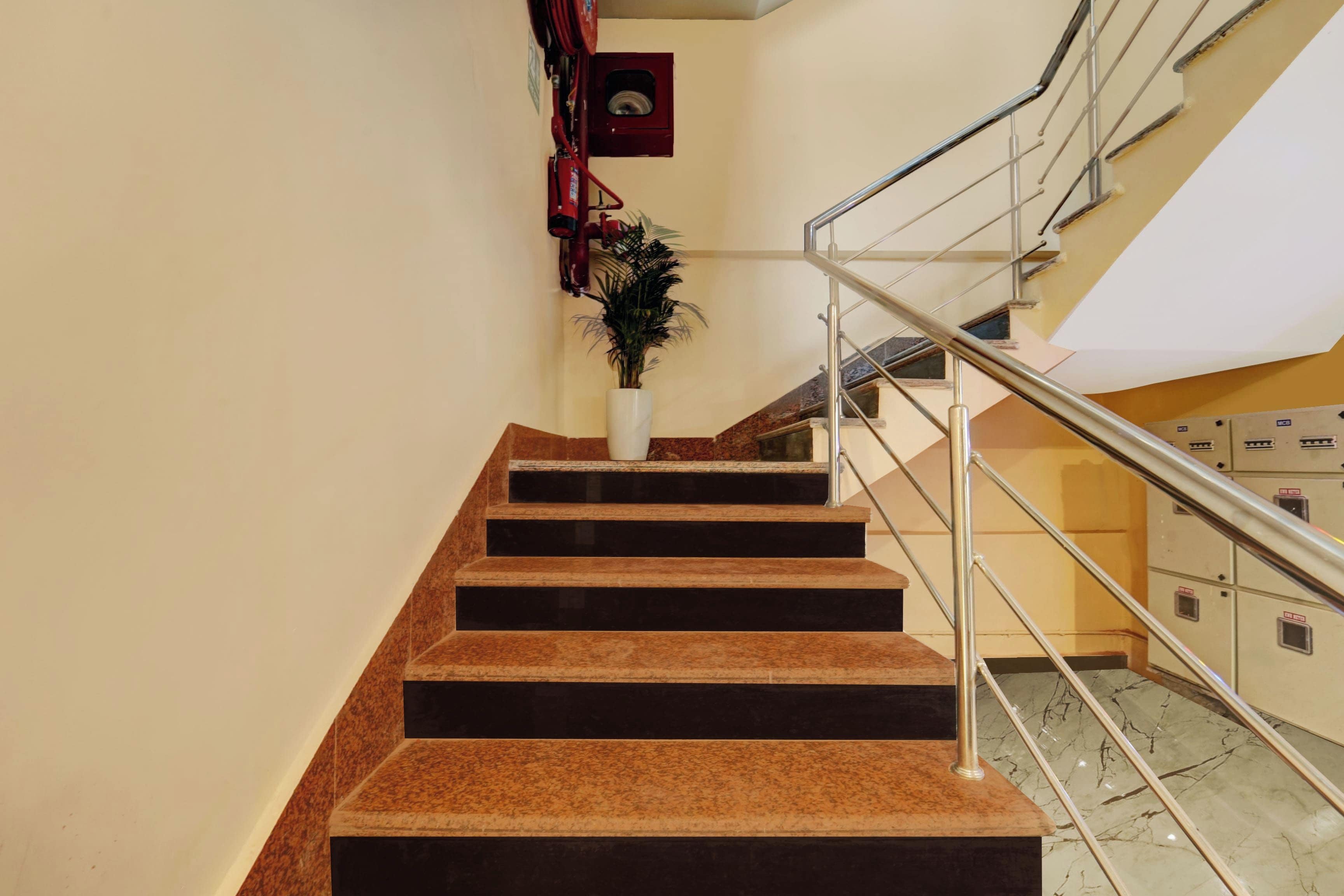 Una escalera con barandilla metálica, una planta en maceta y un extintor en la pared.