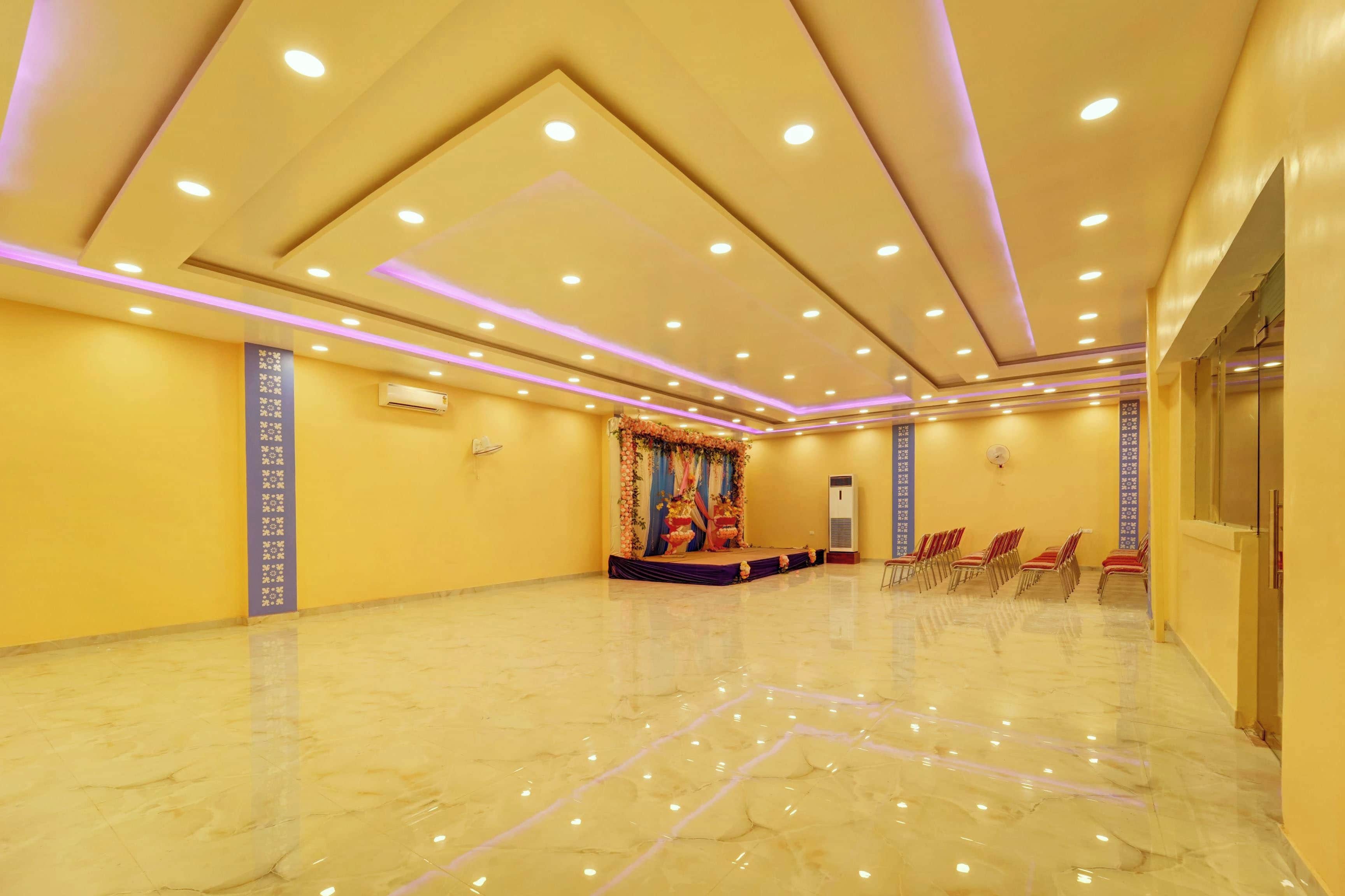 Un amplio salón con piso de mármol pulido, luces empotradas en el techo y un escenario con decoraciones florales.