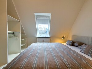 A bedroom with a sloped ceiling, a bed with striped bedding, a bedside lamp, and a window with a view. - Holiday Apartment With 1 Bedroom (Wyk auf Foehr)