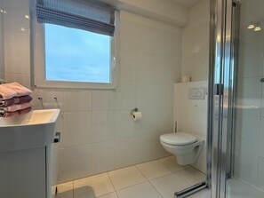 A modern bathroom with a glass shower enclosure, a toilet, and a sink with a towel stack. - Holiday Apartment With 1 Bedroom (Wyk auf Foehr)