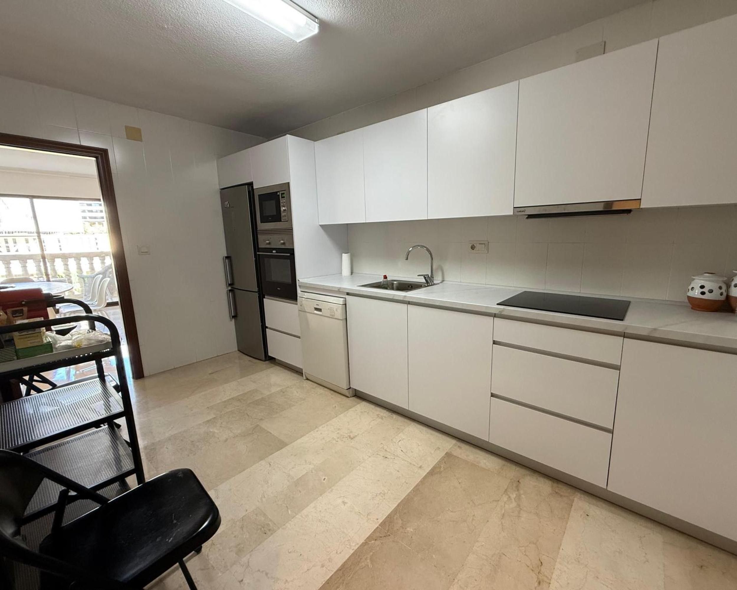 A kitchen with white cabinets, a stainless steel refrigerator, a built-in oven, and a sink.