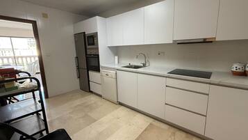 A kitchen with white cabinets, a stainless steel refrigerator, a built-in oven, and a sink.
