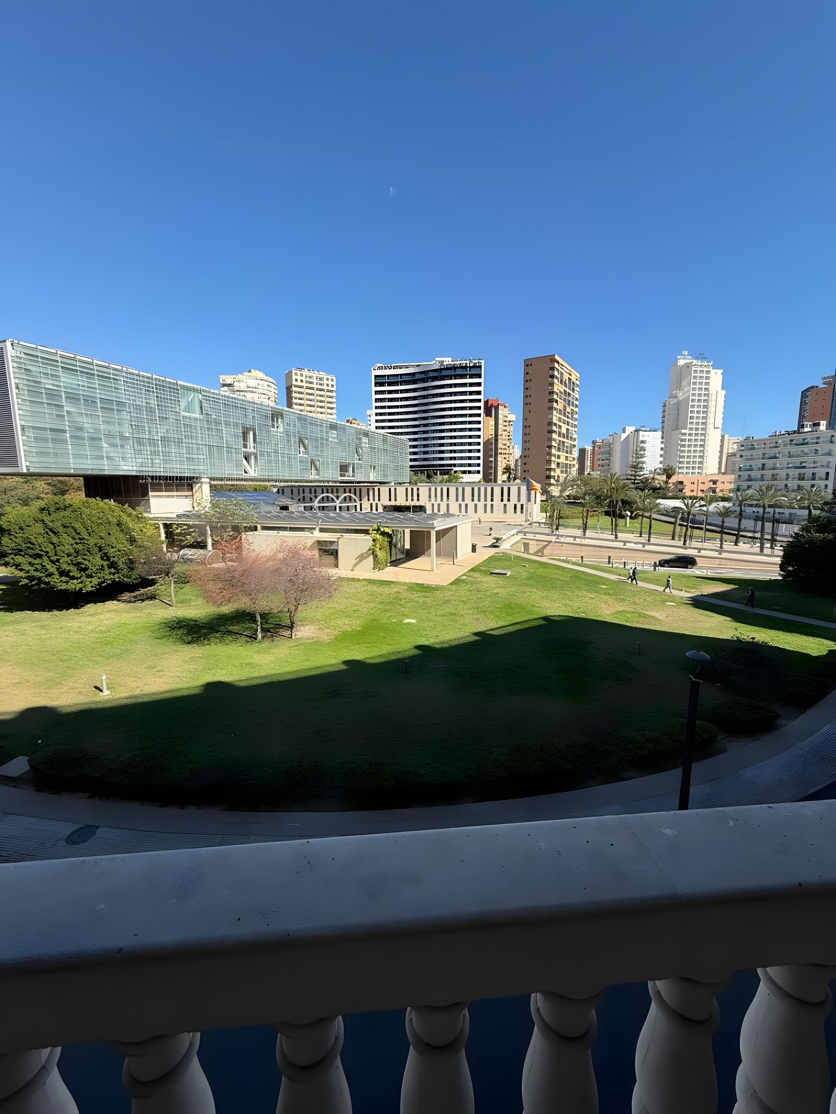 A cityscape with modern buildings, a grassy area, and a clear sky.