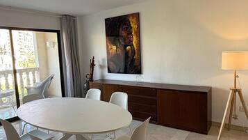 A modern dining area with a round table and chairs, a painting on the wall, and a lamp on a tripod.
