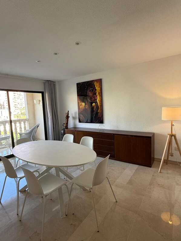 Un espace de salle à manger moderne avec une table ronde et des chaises, un tableau accroché au mur et une lampe sur un trépied.