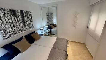 A hotel room with a large bed, a desk, and a chair. There is a large painting on the wall and a mirror.