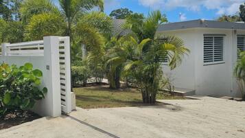 A gated entrance with a concrete pathway leading to a building with a white exterior and a window with horizontal blinds.