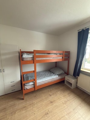 Ein Stockbett mit Schrank und kleinem Nachttisch in einem Zimmer mit Holzboden.