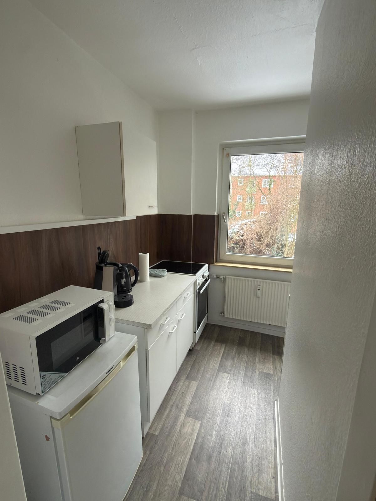 A compact kitchen with a microwave, kettle, and a window with a view of buildings.