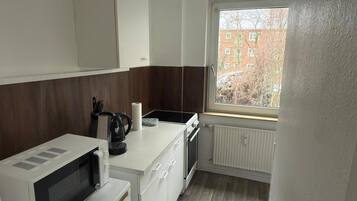 A compact kitchen with a microwave, kettle, and a window with a view of buildings.