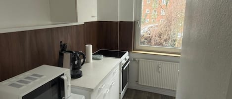 Cocina compacta con microondas, hervidor y ventana con vistas a edificios.