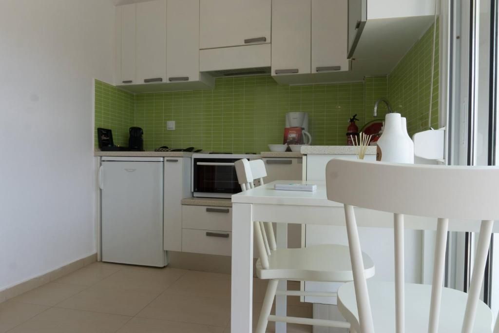 Una cocina compacta con armarios blancos, un refrigerador pequeño, un microondas y una cafetera.