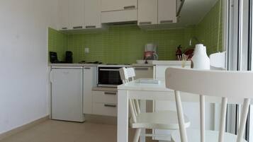 Una cocina compacta con armarios blancos, un refrigerador pequeño, un microondas y una cafetera.