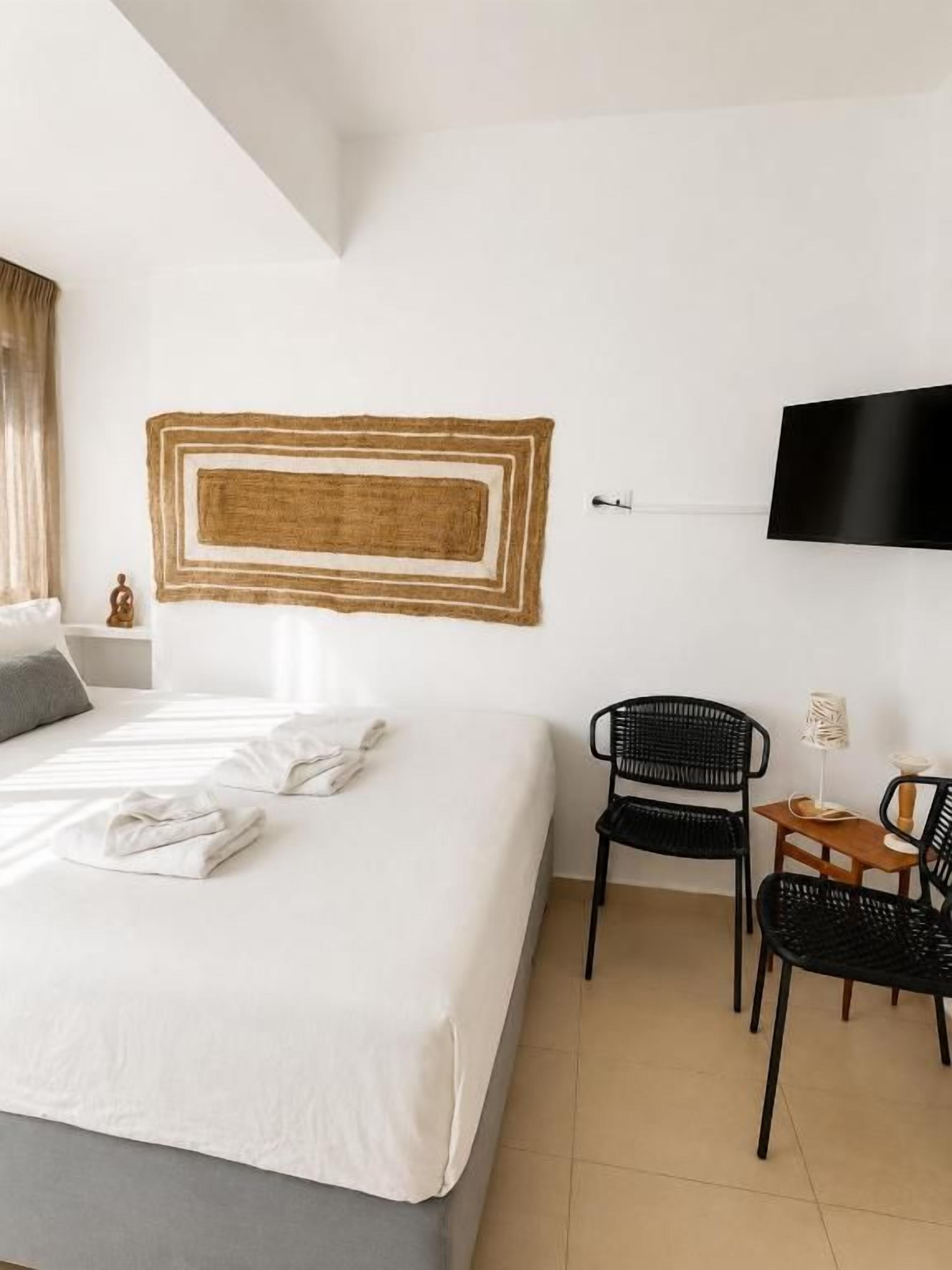 Una habitación de hotel con una cama, un televisor de pantalla plana montado en la pared y dos sillas negras.