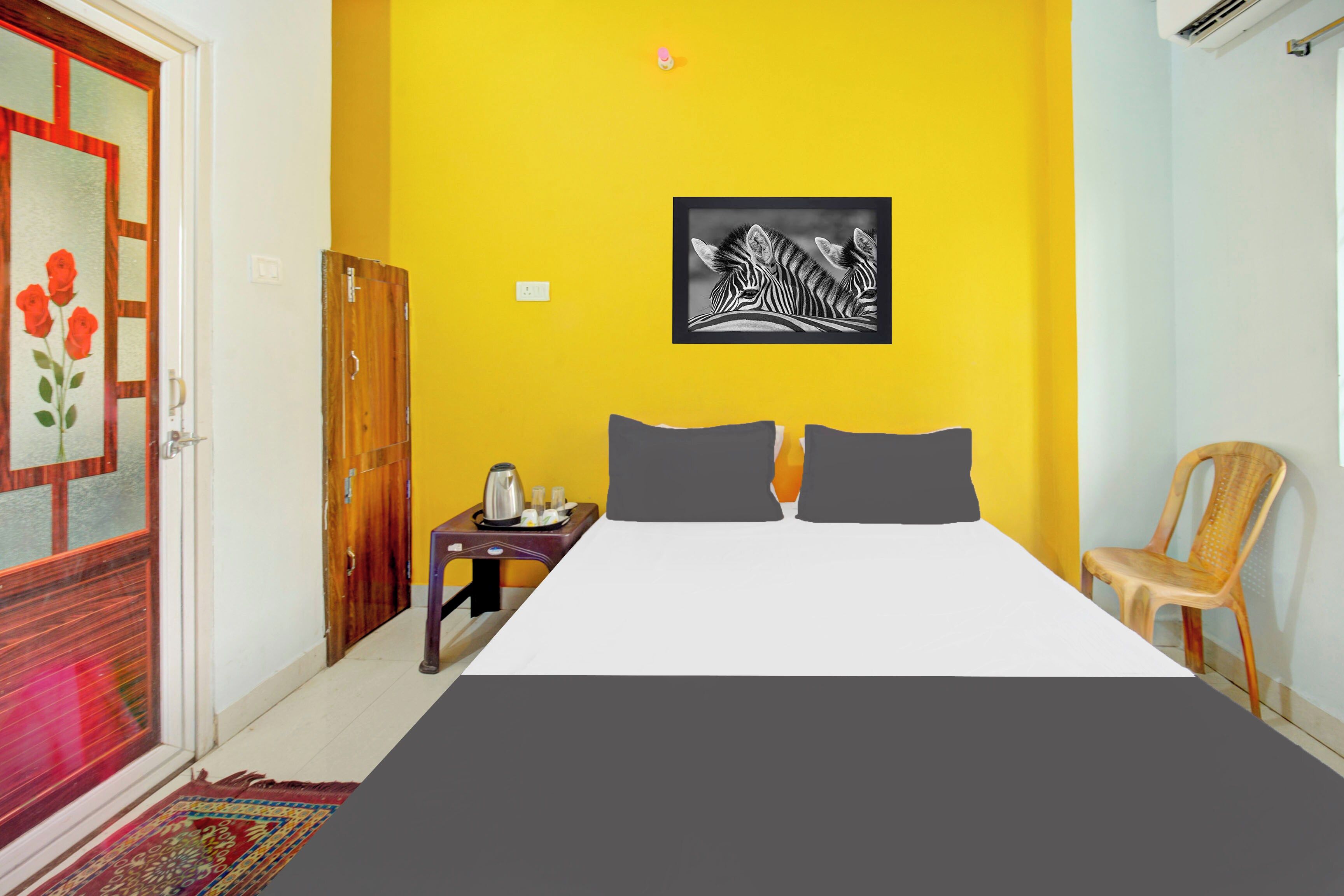 A room with a bed, a small table with a kettle, a chair, and a door with a floral design.