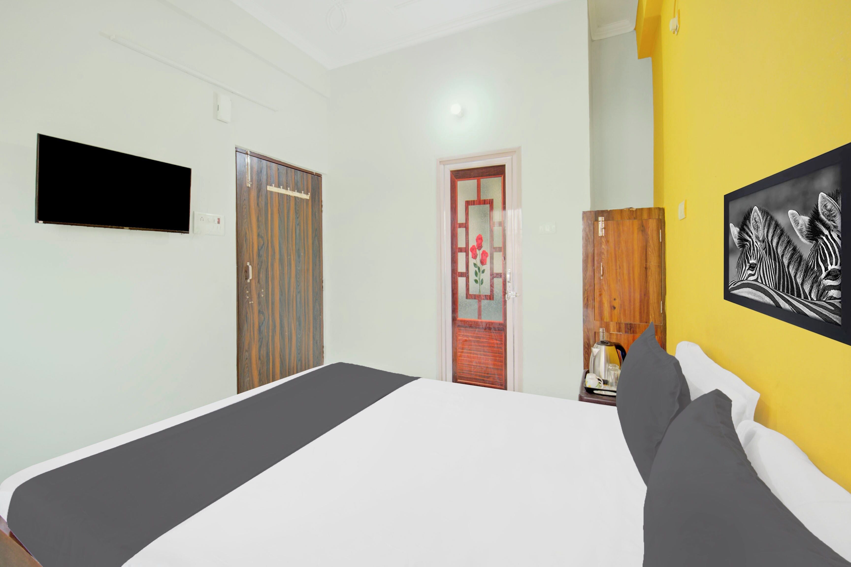 Un dormitorio con una cama, un televisor montado en la pared, un armario y una puerta con picaporte rojo.