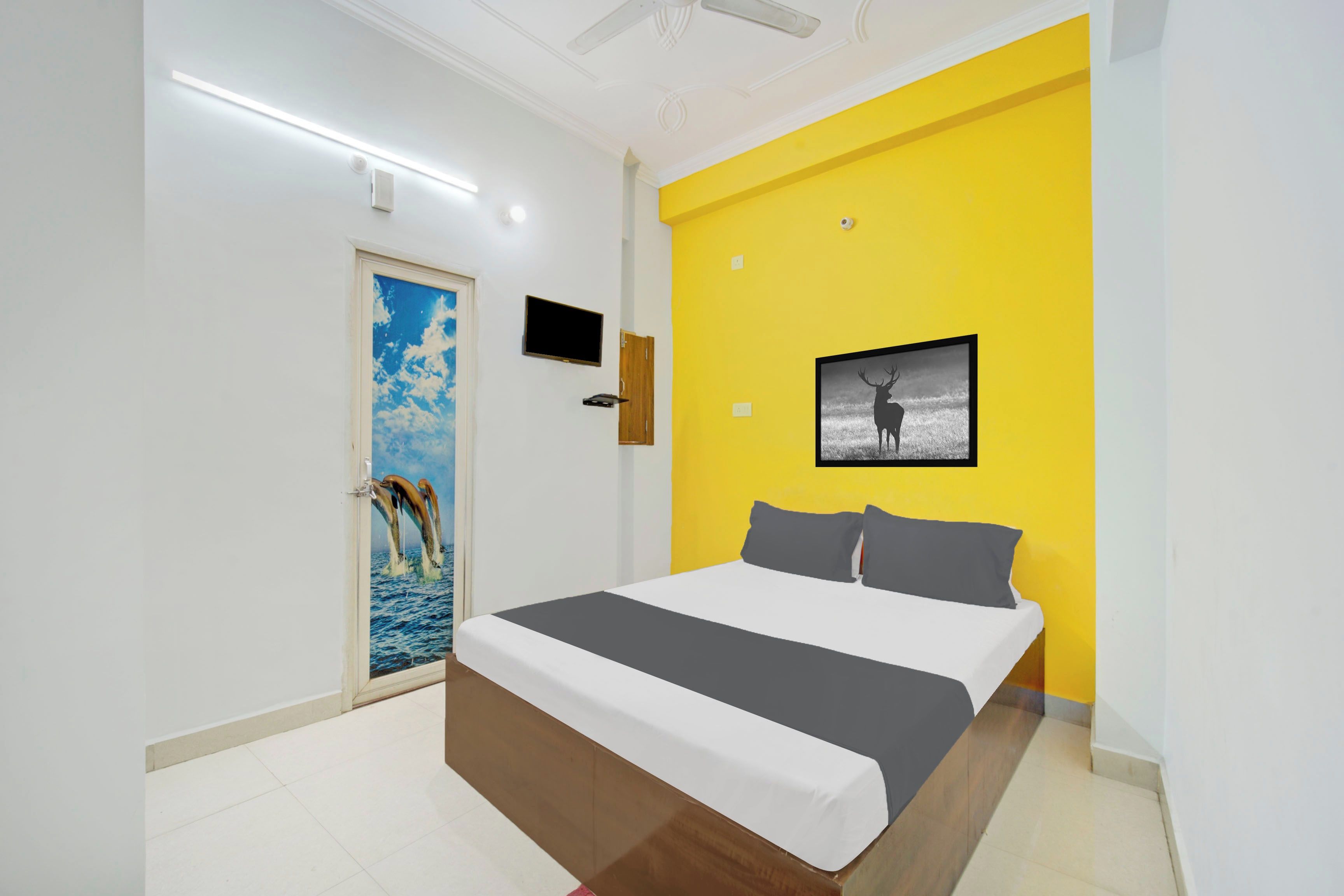 A bedroom with a bed, a television, a door with a painting, and a yellow wall.