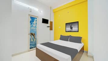Un dormitorio con una cama, un televisor, una puerta decorada con un cuadro y una pared amarilla.