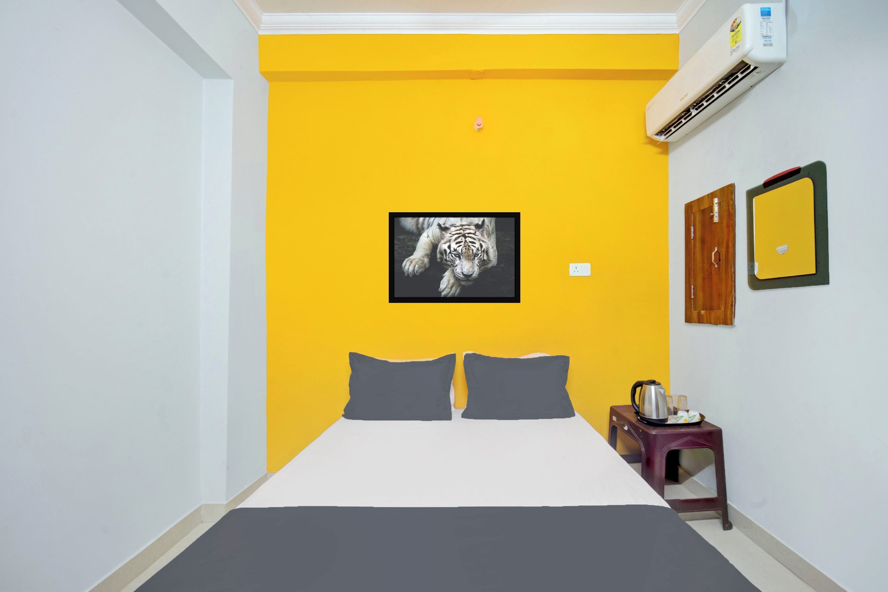 A hotel room with a bed, a picture of a tiger, an air conditioning unit, a mirror, and a small table with a kettle.