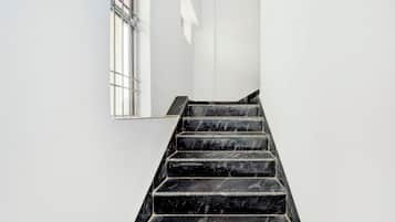 A staircase with black steps leading upwards, white walls, and a window with metal bars.