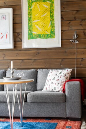A grey sofa with a patterned pillow, a small round table with a candle, and a floor lamp. - FA1084 Mountain retreat in Trysil, Sauna, 8 people (Trysil)
