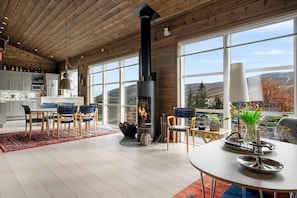 A modern interior with a fireplace, dining area, and large windows offering a view of the outdoors. - FA1084 Mountain retreat in Trysil, Sauna, 8 people (Trysil)