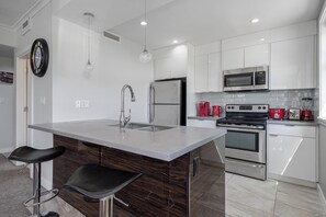 Una cocina moderna con una isla central, electrodomésticos de acero inoxidable y taburetes de bar.